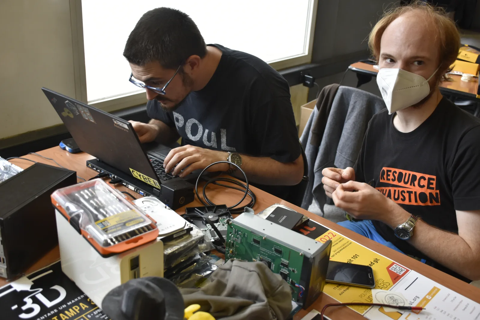 Dos personas trabajando en una laptop con GNU/Linux junto a discos y kits de reparacion